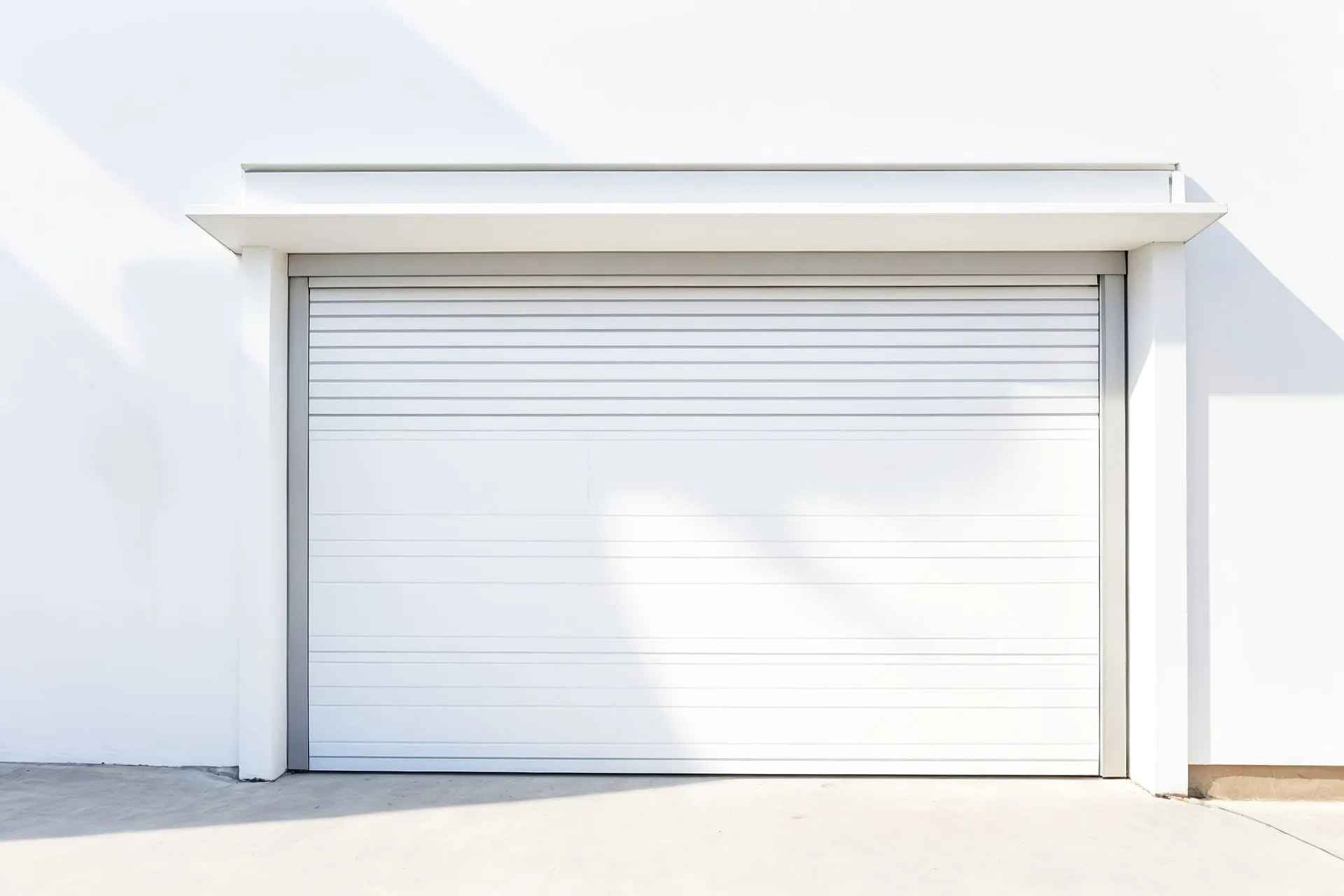 A white garage door is sitting on the side of a white building.