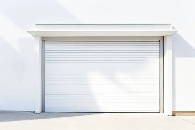 A white garage door is sitting on the side of a white building.