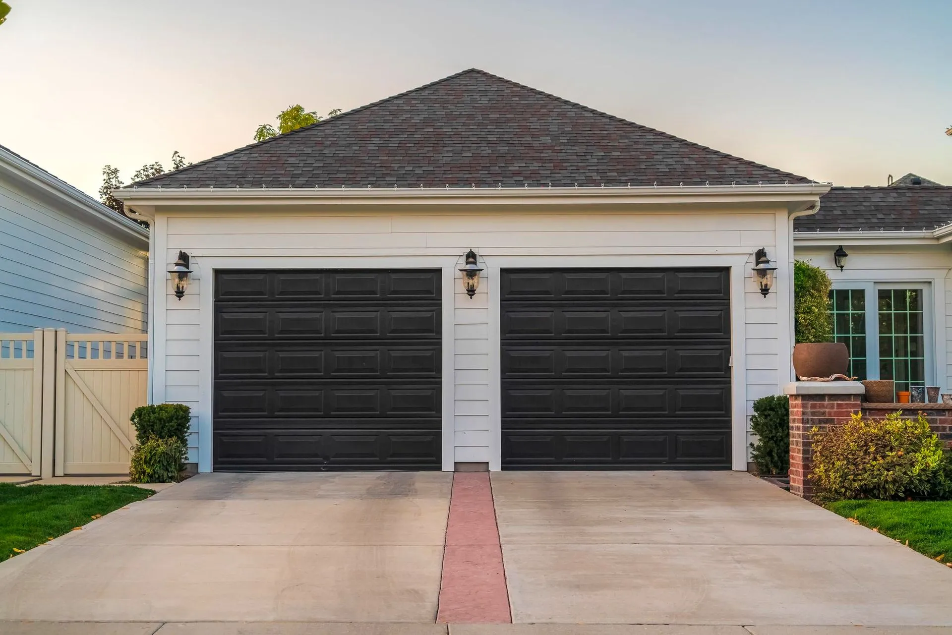A white house with two black garage doors and a driveway.